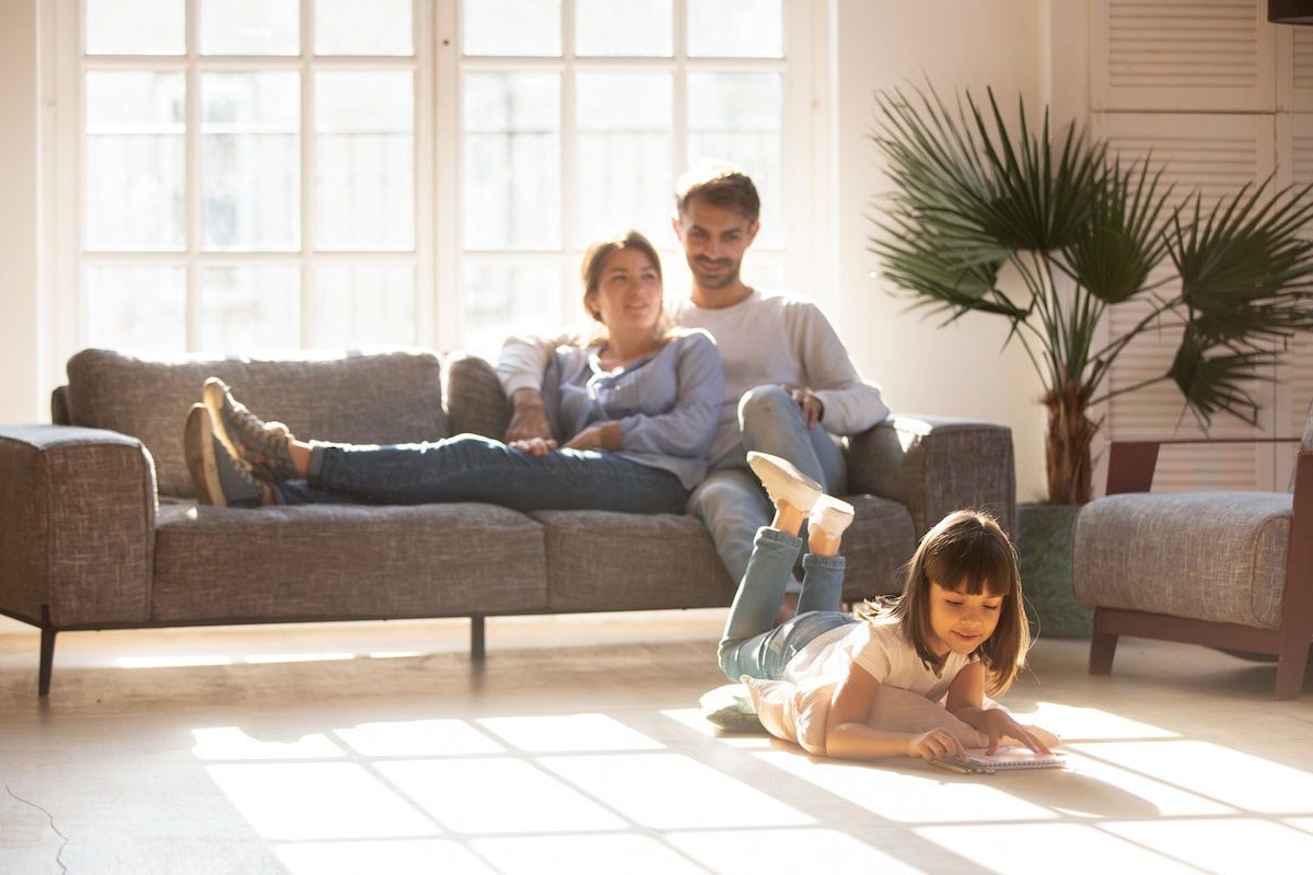 A man and a woman lying on the couch with a child colouring in while on the floor