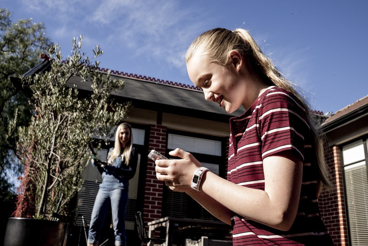 Teenage girl on phone in backyard with mum in background