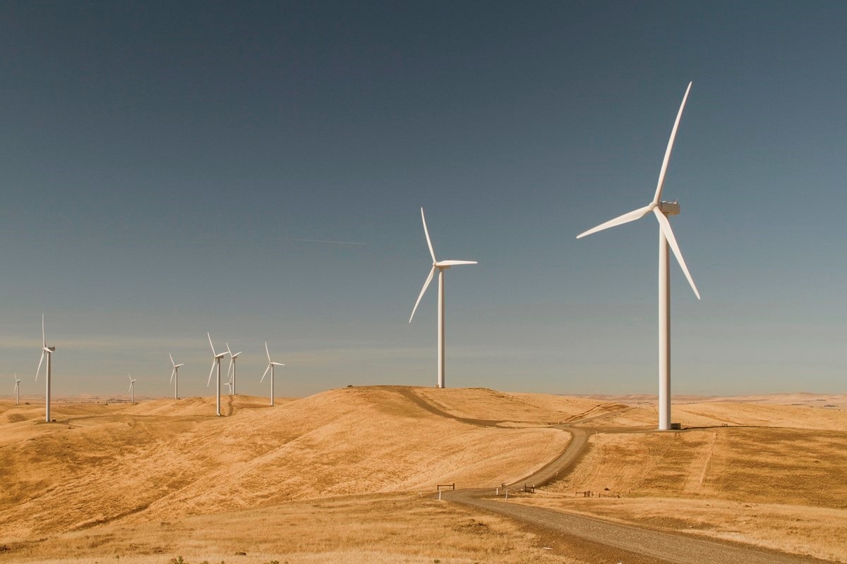 View of Macarthur Wind Farm featuring multiple wind turbines standing tall on a dry grassy landscape with a clear blue sky in the background.