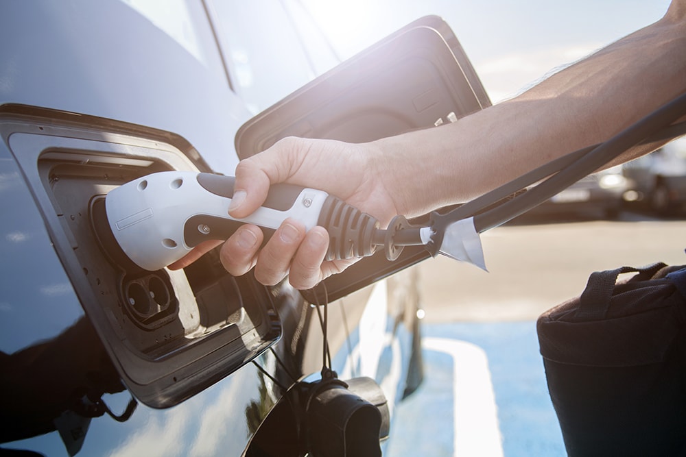 Color image of a man's hand preparing to charge an electric car.