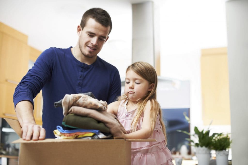 A young child helping her dad pack boxes full of clothes