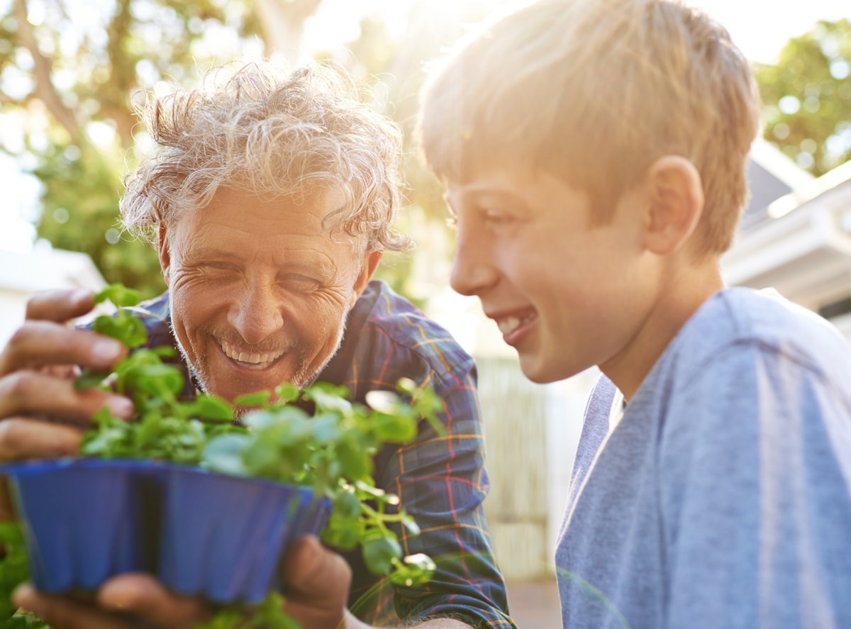 Smiling father and son outside planting herbs