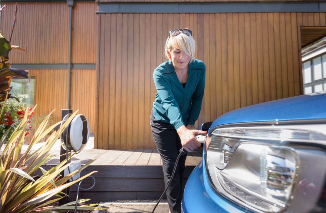 Woman plugging charger into EV in front of garage