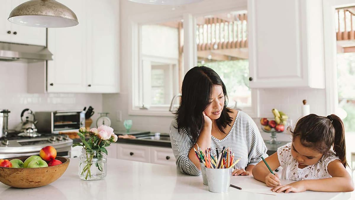 Mother watching daughter drawing while both sitting at kitchen bench