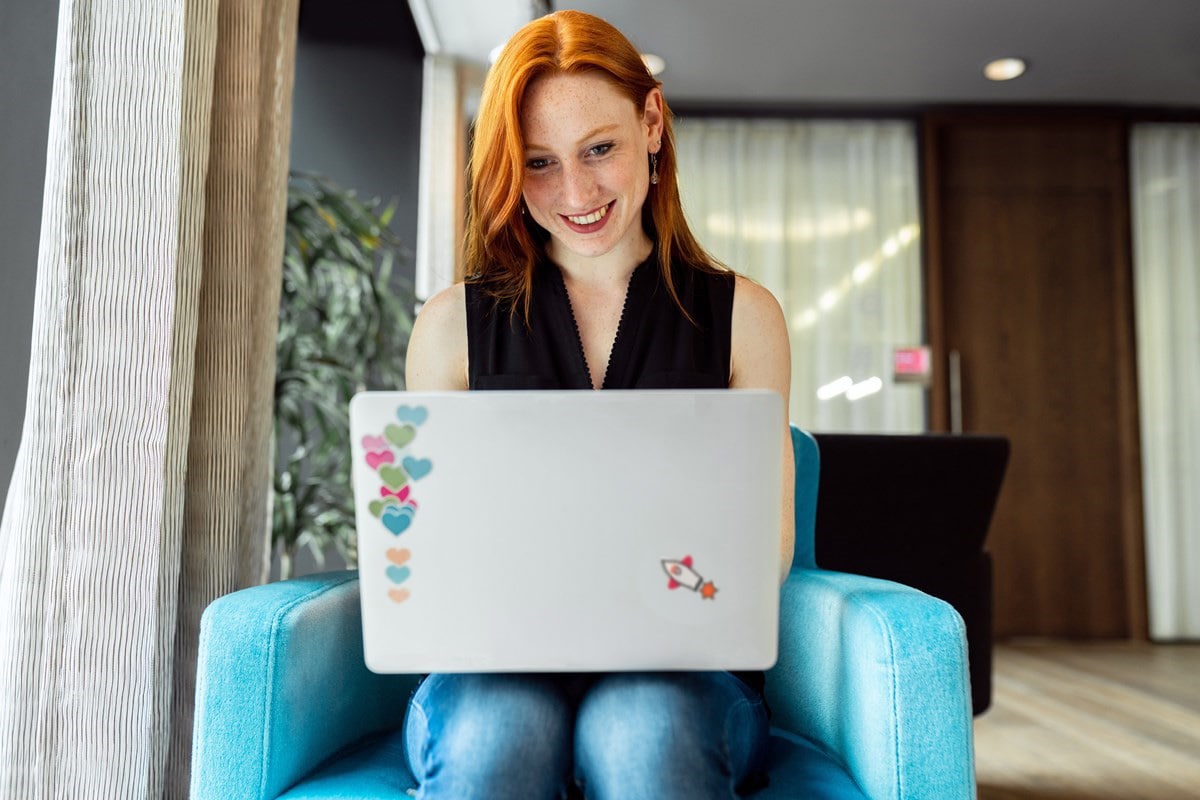 Photo of an employee working on their laptop on a bright blue couch.  