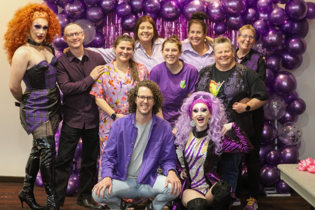 AGL team members celebrating 'Wear it Purple Day' with vibrant outfits and drag performers.