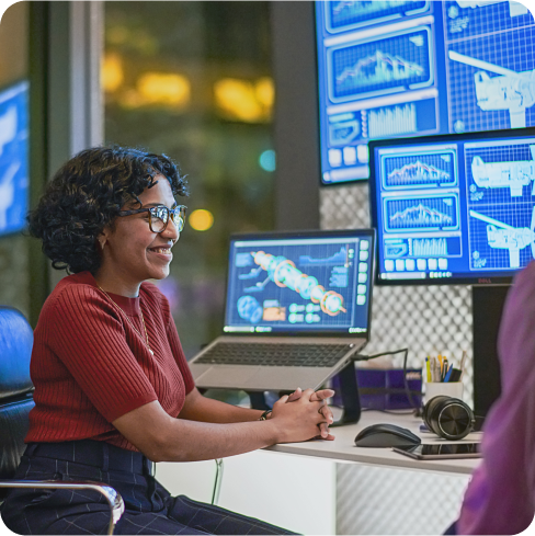 An individual in a red shirt is seated in front of multiple monitors displaying graphs and data in a design space.