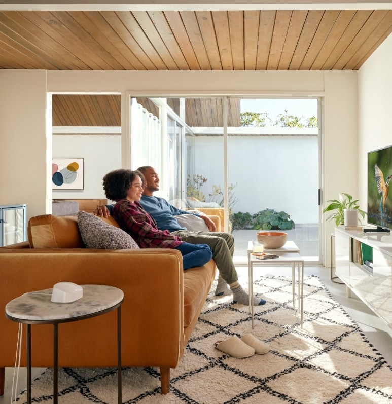 Two people on a couch streaming video to their TV with an eero modem on the table in the foreground.