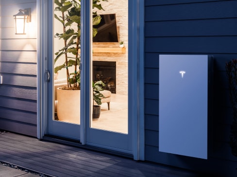 Tesla Powerwall 3 battery attached to the outside of a house at night.