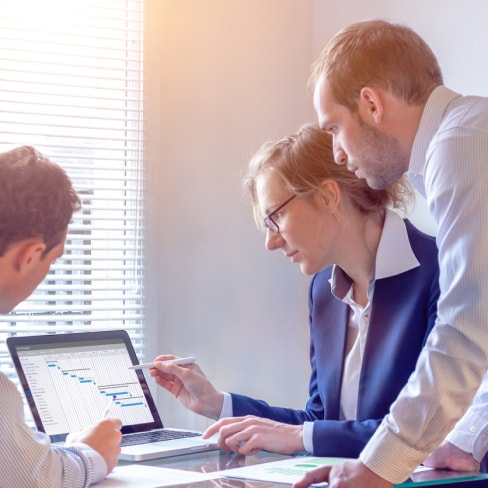 Three office workers standing around and looking at a chart on a laptop