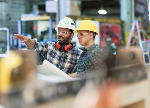 Two coworkers having a discussion in a factory, foreground blurred